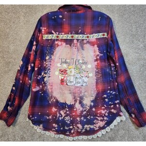 May include: A long-sleeve button-down flannel shirt in red and blue plaid with a bleached center panel. The back features a floral graphic in jars with the text Today I Choose Faith Hope Love Joy, a floral trim strip, and a white lace hem border.