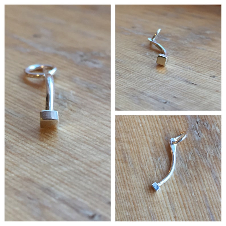 May include: A silver charm with a curved shape and a square at the end. The charm has a loop at the top for attaching to a bracelet or necklace.
