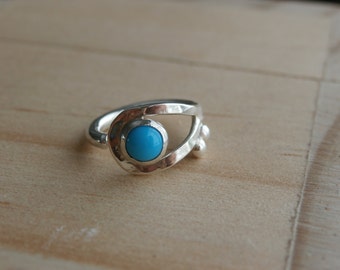 May include: A silver ring with a turquoise stone set in a unique, abstract design. The ring has a textured finish and a delicate, openwork design.