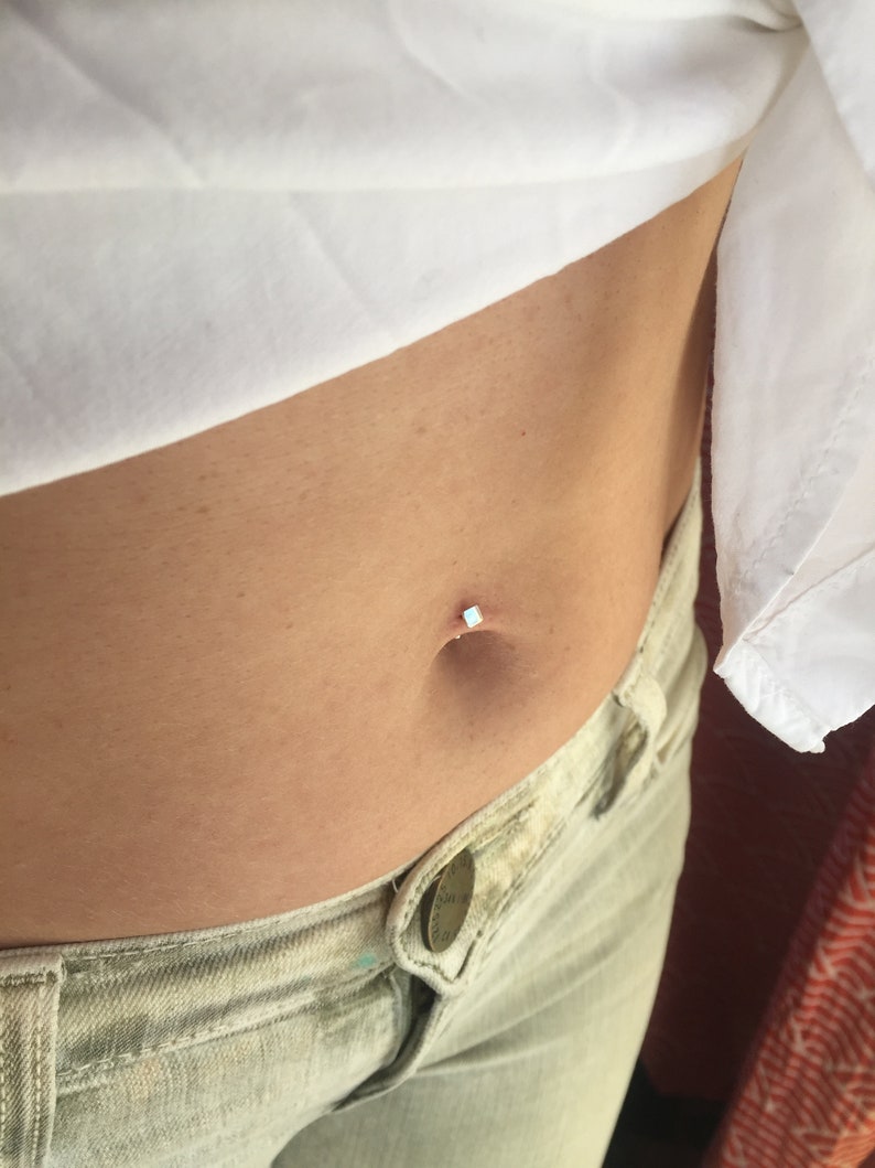 May include: A close-up of a person's midsection with a small, clear belly button ring. The ring is set with a tiny, white stone.