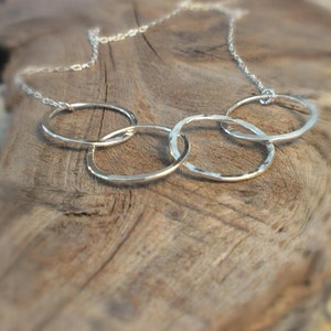 May include: A silver necklace with five interconnected circles, each with a hammered texture. The necklace is displayed on a wooden surface.