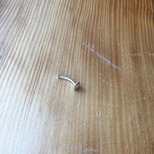 May include: A silver nose ring with a small, flat, rectangular stud.