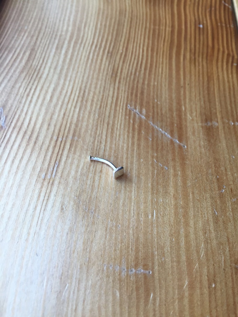 May include: A silver nose ring with a small, flat, rectangular stud.