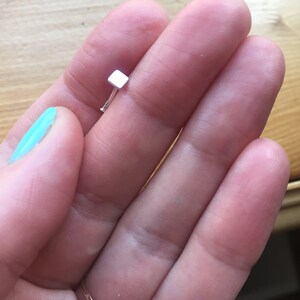 May include: A silver nose ring with a small square-shaped stud.