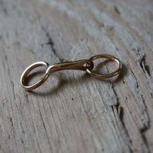 May include: A gold-colored metal snaffle bit charm with a round ring on one end.