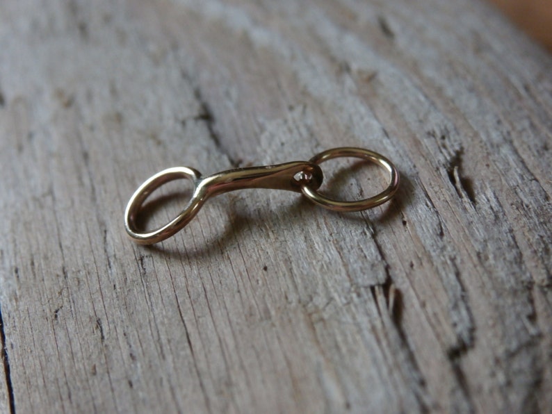 May include: A gold-colored metal snaffle bit charm with a round ring on one end.