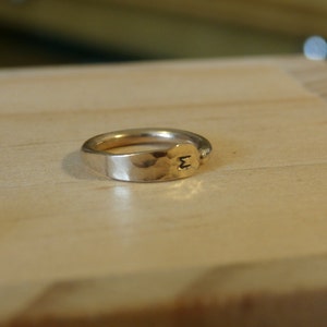 May include: A gold-toned ring with a hammered finish and the letter "M" engraved on the side.