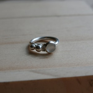 May include: A silver ring with a white stone and three silver beads.