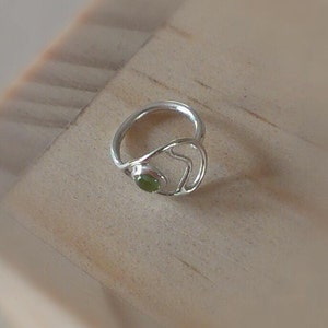 Op de afbeelding: Een zilveren ring met een groene edelsteen in een hartvormig ontwerp.