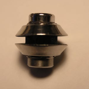 May include: A silver metal object with a round top and a ring around the middle. The object has a small hole in the center.