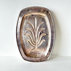 May include: An antique silver-plated serving tray with an oval shape and a decorative floral design in the center. The tray has a tarnished finish, giving it a vintage appearance. The tray is ideal for serving food or as a decorative piece.
