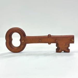 May include: A wooden key-shaped wall-mounted key holder. The key holder is made of stained wood and features a large keyhole design on the head. It has several pegs for hanging keys. The key holder is approximately 12 inches long.