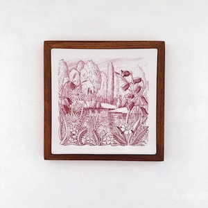 May include: A square ceramic tile framed in dark brown wood featuring a maroon ink illustration of a pond surrounded by tall trees and various wildflowers including bell-shaped blossoms and daisies in a detailed, etched line art style.