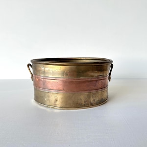 Peut inclure: Un pot de fleurs vintage en métal avec un bord et des poignées en laiton. Le pot de fleurs présente une bande de cuivre au milieu, avec du laiton en haut et en bas. Le pot de fleurs est rond et a un aspect vieilli.