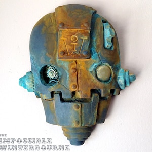 May include: A steampunk-style wall sculpture in shades of blue and rust. The piece resembles a robot head with visible gears, rivets, and the text "The Impossible Winterbourne". The sculpture has a weathered, aged appearance.