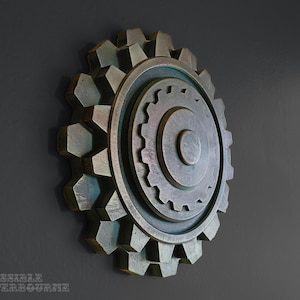 May include: A bronze-colored gear wall decor with a layered design. The gear features a large outer ring with hexagonal teeth, a middle ring, and a central circular element. The wall decor is mounted on a dark gray wall.