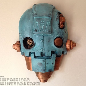 May include: A teal and copper-colored steampunk-style wall sculpture in the shape of a robot head. The sculpture features visible gears, rivets, and the text "The Impossible Winterbourne" at the bottom.