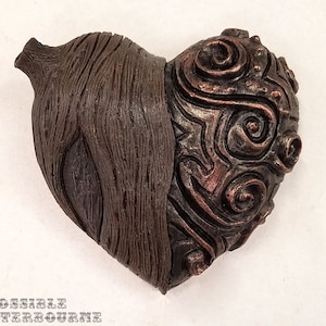 May include: A heart-shaped sculpture with a textured, wood-like finish on one side and a swirling, copper-colored design on the other side.