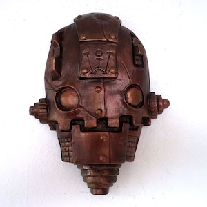 May include: A bronze-colored robot head sculpture with a detailed design and a Roman numeral 'VII' on the forehead.