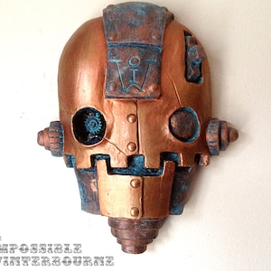 May include: A copper and blue robot head sculpture with a gear in one eye and a stylized letter 'W' on the forehead.