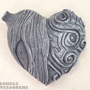 May include: A gray heart-shaped sculpture with a textured, wood-like surface on one side and a swirling, abstract design on the other side.