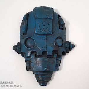 May include: A blue robot head sculpture with a metal texture and a Roman numeral 'IV' on the forehead. The sculpture has a detailed design with gears and rivets.