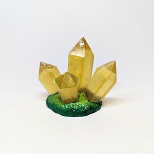 May include: A cluster of four golden crystals with glitter embedded in the resin, set on a green base.