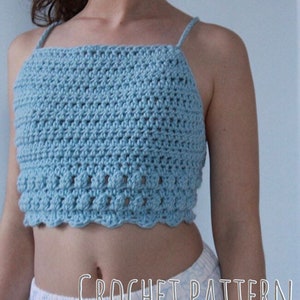 May include: A light blue crochet crop top with a scalloped hem. The top is made with a simple stitch pattern and has thin straps. "CROCHET PATTERN" is written in white text at the bottom of the image.