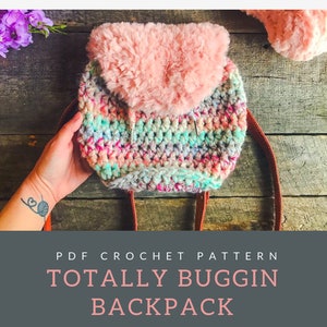 Pode incluir: Uma mochila de crochê com uma aba de pele sintética rosa. A mochila é feita com um fio multicolorido com tons de rosa, azul, verde e branco. A mochila tem uma alça de couro marrom. O texto na imagem diz "PDF CROCHET PATTERN TOTALLY BUGGIN BACKPACK".