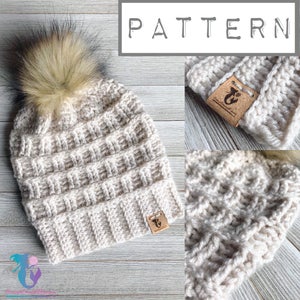 Puede incluir: Un gorro de punto de ganchillo con un pompón esponjoso en la parte superior. El gorro es de color beige claro y tiene un patrón de puntadas texturizado. El gorro tiene una etiqueta de cuero marrón con un logotipo.