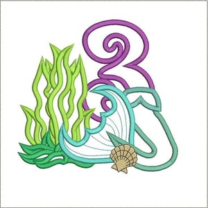 May include: An embroidered design featuring a seashell, seaweed, and a stylized wave in shades of teal, green, and purple. The design is set against a white background, evoking a nautical theme.