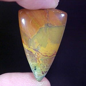 May include: A teardrop-shaped cabochon of polished agate with a mix of orange, yellow, green, and brown colors.