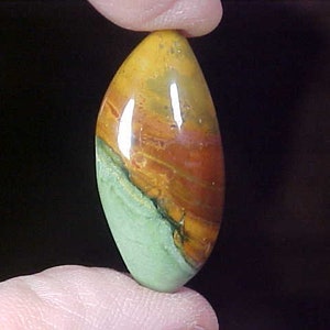May include: A smooth, polished, oval-shaped gemstone with a mix of green, yellow, orange, and red colors. The stone has a swirling pattern of colors.