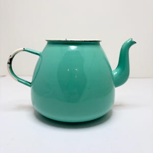May include: A round, turquoise enamel teapot with a wide base and a curved spout. The teapot features a white rim and a matching handle, both showing signs of wear with black metal exposed along the edges, giving it a distressed appearance.