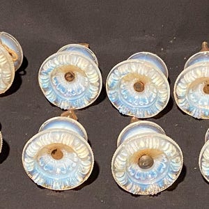 May include: A set of seven round, translucent opalescent glass drawer knobs featuring a molded floral petal pattern. Each knob has a central metal screw attachment extending from the back, with a milky white and iridescent blue finish.