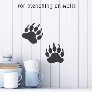 Puede incluir: Dos plantillas negras de huellas de oso en una pared blanca. El texto "for stenciling on walls" est&aacute; encima de las huellas. Un tarro azul claro, tazas blancas y una taza azul claro est&aacute;n en primer plano.