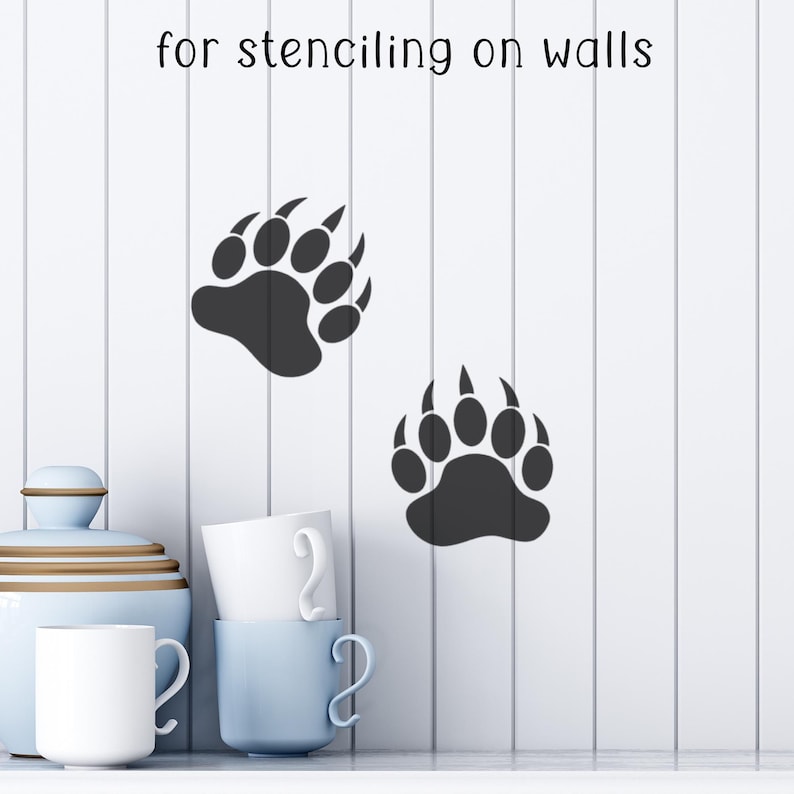 Puede incluir: Dos plantillas negras de huellas de oso en una pared blanca. El texto "for stenciling on walls" est&aacute; encima de las huellas. Un tarro azul claro, tazas blancas y una taza azul claro est&aacute;n en primer plano.