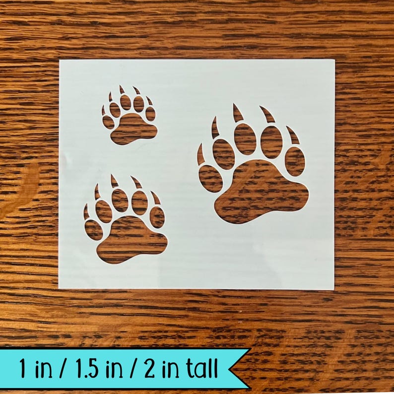 Puede incluir: Un est&eacute;ncil blanco con tres huellas de patas de oso marrones de diferentes tama&ntilde;os. El texto en la parte inferior dice "1 in / 1.5 in / 2 in tall". Las medidas son de aproximadamente 2,5 cm, 3,8 cm y 5 cm de alto.