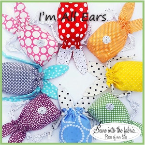 May include: A collection of colorful fabric bunny bags with polka dot patterns. The bags are arranged in a circle with the text "I'm All Ears" at the top and "Sewn into the fabric... Pieces of our lives" at the bottom.