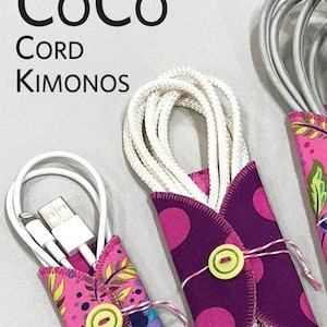 May include: Three cord organizers in varying sizes. Each features a colorful fabric wrap with a button closure. The fabrics include a purple polka dot pattern and a pink floral design. The organizers are designed to hold cords, cables, and more.