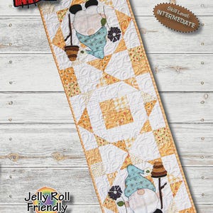 May include: A Spring Bee Gnome table runner quilt pattern by Patch Abilities, Inc. labeled P288. The rectangular design measures 12 1/2 inches by 36 inches and features two gnomes with blue hats, bees, and flowers on a white and yellow background.