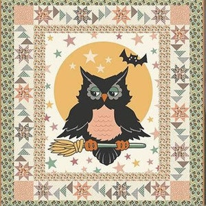 May include: A Halloween-themed quilt featuring a central image of a black owl with a peach-colored chest, holding a broom against a yellow moon background. The quilt has a decorative border with stars, triangles, and floral patterns in shades of peach, green, and cream.