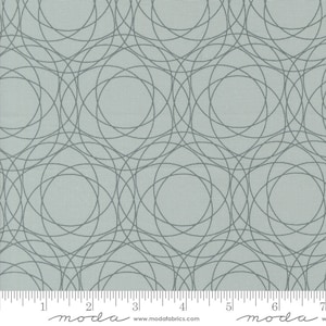 May include: A light blue fabric with a repeating pattern of overlapping gray circles. The fabric is textured and has a subtle sheen. The fabric is marked with a ruler in inches and the words "moda" and "www.modafabrics.com".