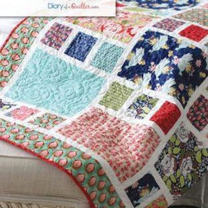 May include: A colorful patchwork quilt with a variety of floral and geometric patterns. The quilt is made in a "craftsman" style and is a pattern by Amy Smart. The quilt is displayed on a white couch.