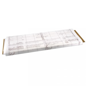 May include: White fabric with a grid pattern and the text "QuiltSmart" and "Mondo Egg" printed on it. The fabric is rolled up and the edge of the roll is visible.