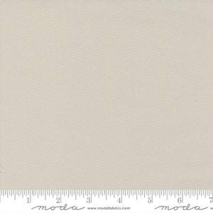 May include: A close-up of a light beige fabric with a subtle texture. The fabric is measured with a ruler that has the word "moda" printed on it.