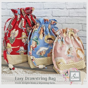 May include: Three drawstring bags with cowboy and cowgirl illustrations. The bags are red, blue, and pink, with a beige polka dot base. The text "Easy Drawstring Bag" and "Fresh designs from a Wyoming farm" are visible.