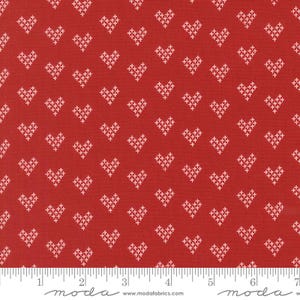 May include: Red fabric with a repeating pattern of white cross-stitch hearts. The fabric has a textured appearance and a ruler is visible along the bottom edge. The fabric is suitable for quilting and crafting projects.