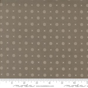 May include: A fabric with a repeating pattern of small, dotted circles and 'X' shapes in a light beige color, set against a solid, muted brown background. The fabric has a textured appearance and a ruler is at the bottom.