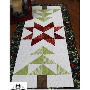 May include: A quilted table runner with the text "Timber Pines" and "Runner: 16" X 40". The runner features a white background with a red star and green tree designs. The border is a dark green floral pattern.